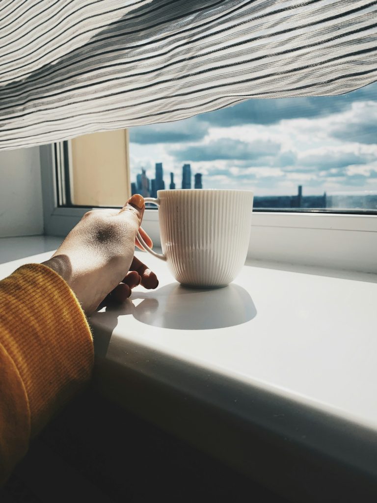 Hands holding a warm cup of tea by a window